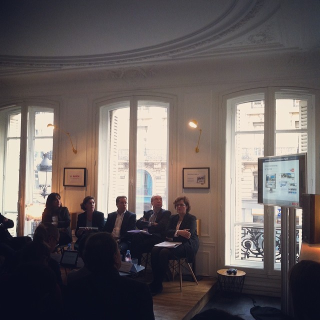 Des clients sont assis dans une grande pièce, à droite de l'image, un écran affiche une présentation