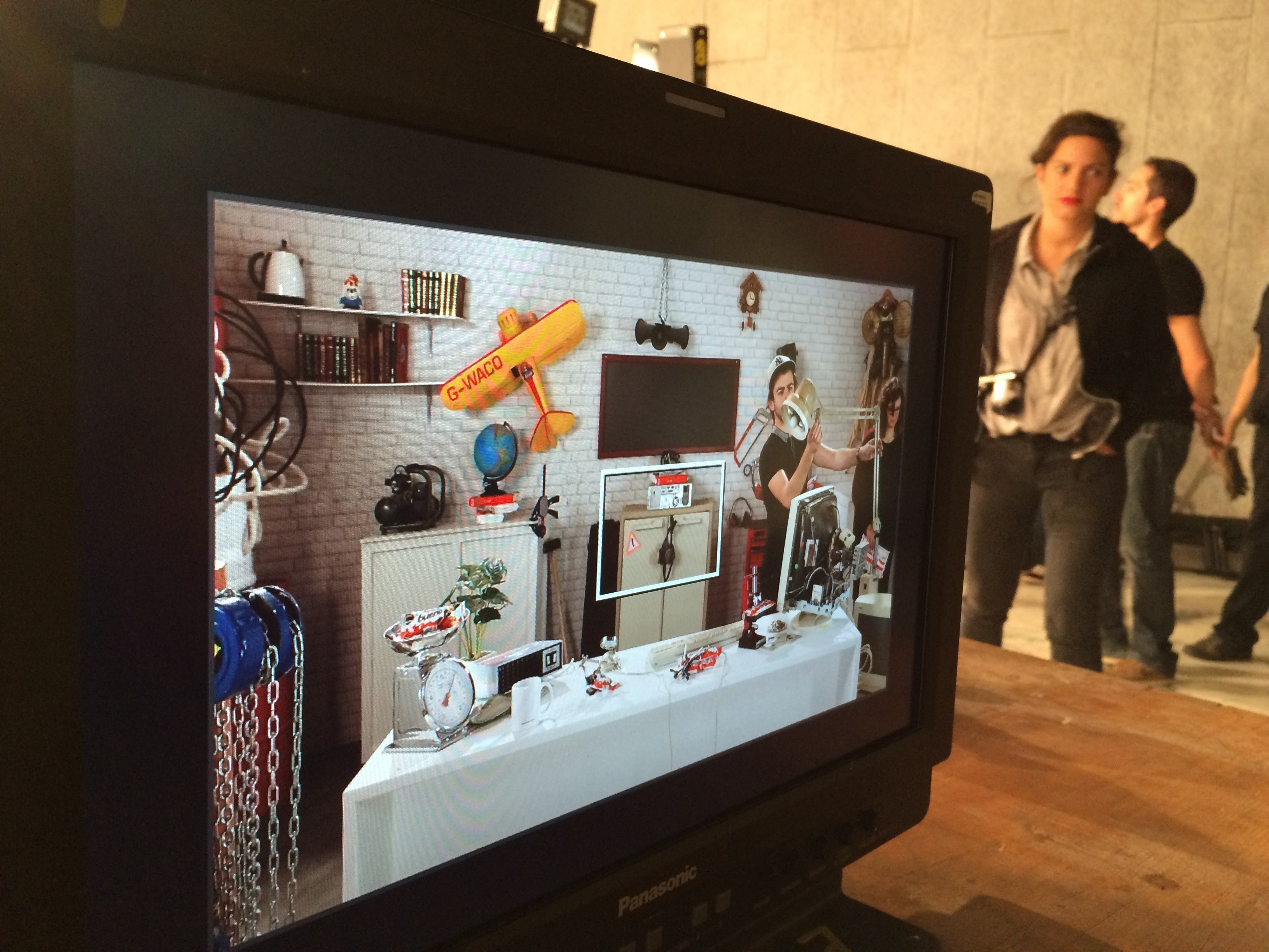 Dans un écran, on voit l'atelier en cours de montage, avec des personnes qui travaillent pour la mise en place du plateau de tournage