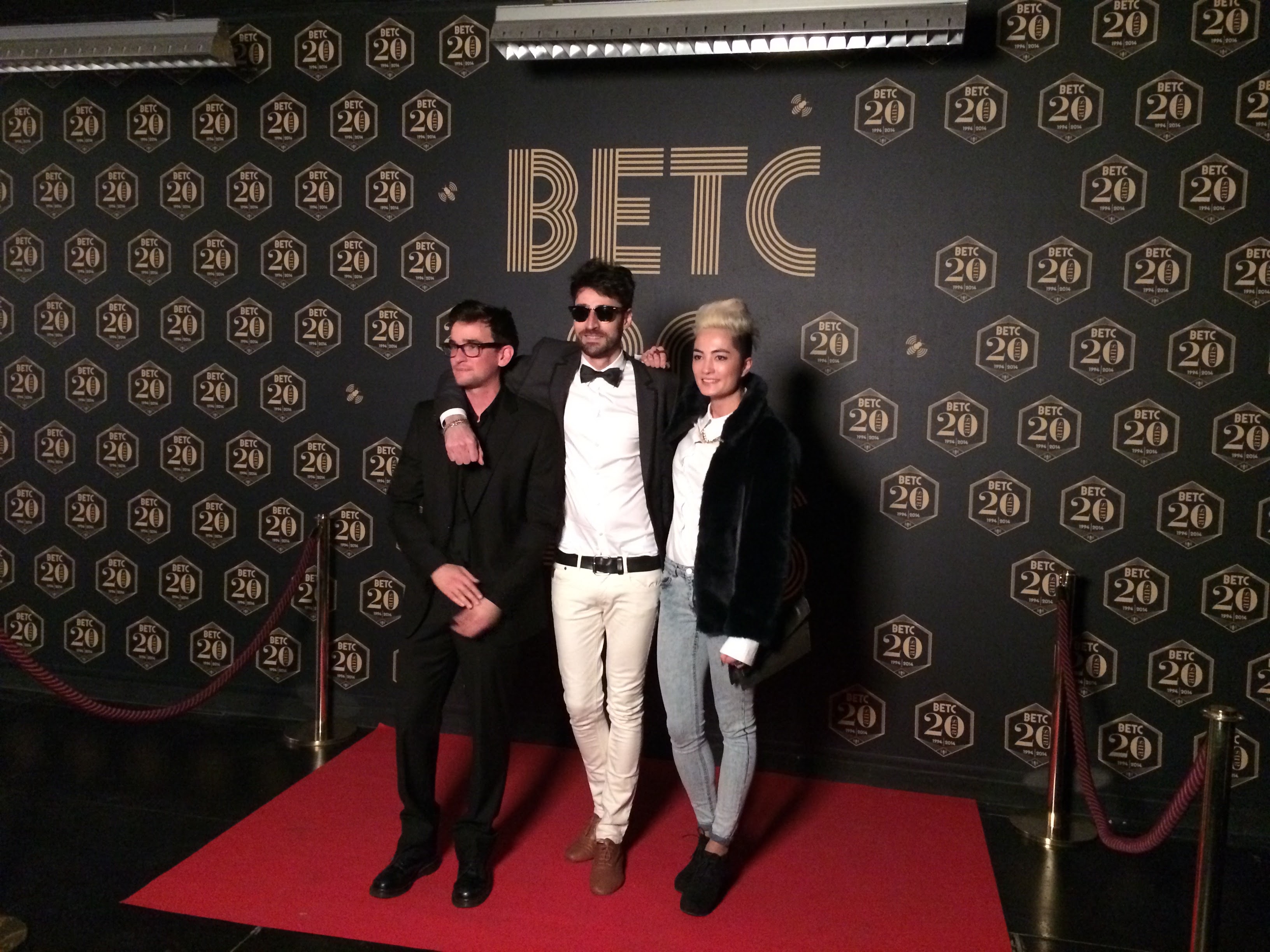 3 personnes posent sur le tapis rouge, derrière eux un mur avec le logo 20 ans de BETC.