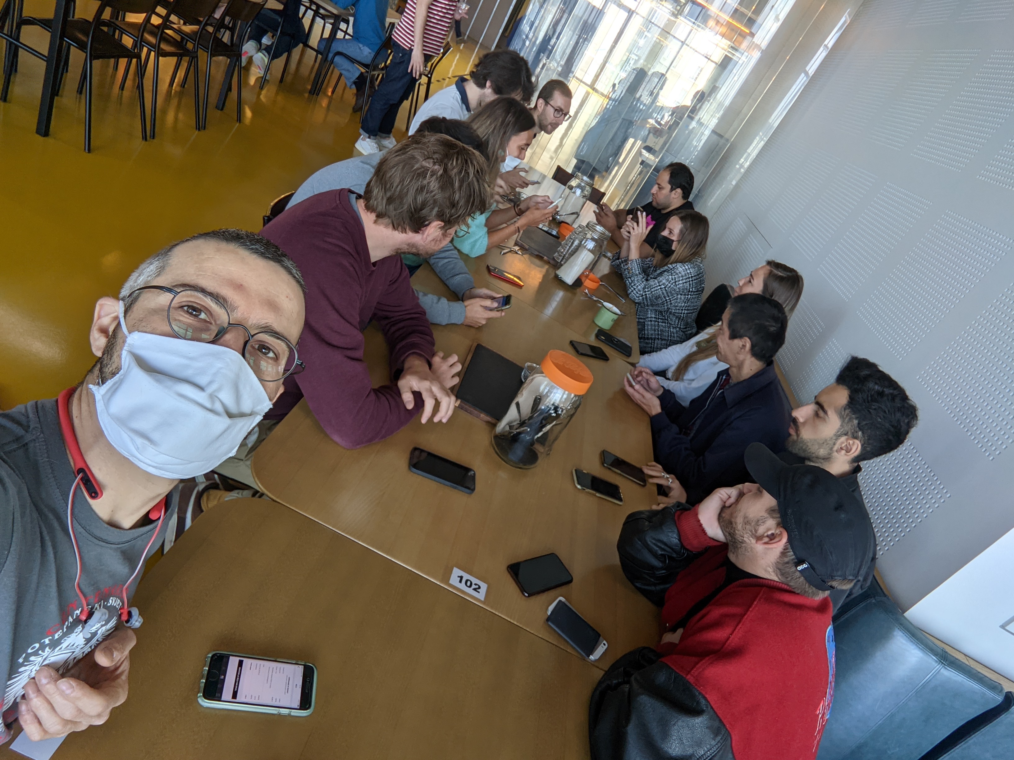 Selfie de groupe autour d’une grande table de restaurant, smartphones et verres posés devant eux.