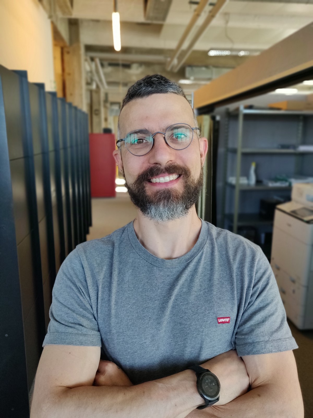 Portrait d’un homme souriant aux bras croisés dans un couloir de bureau.