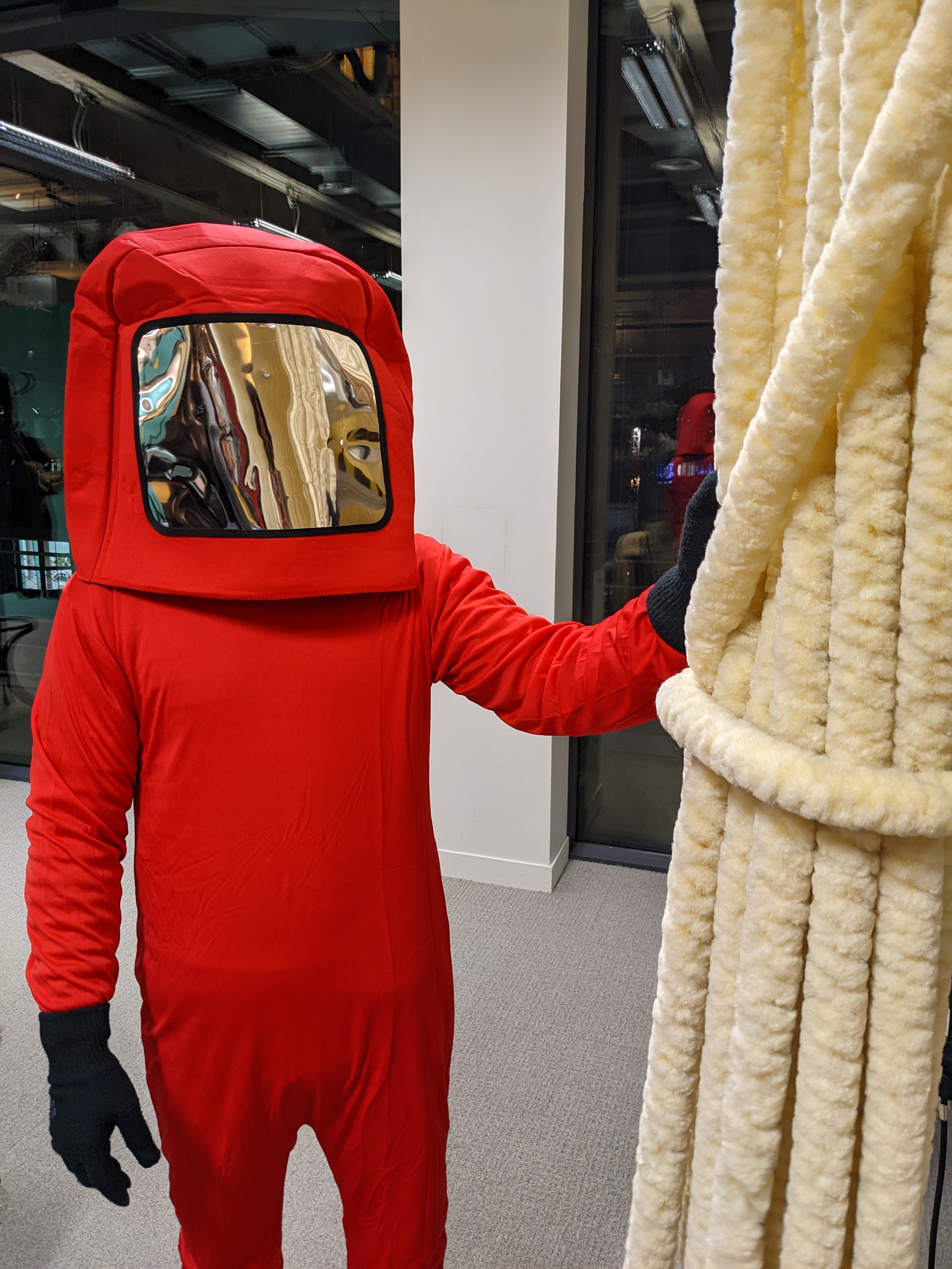 Personne en combinaison rouge intégrale avec visière réfléchissante tenant une structure en mousse claire.