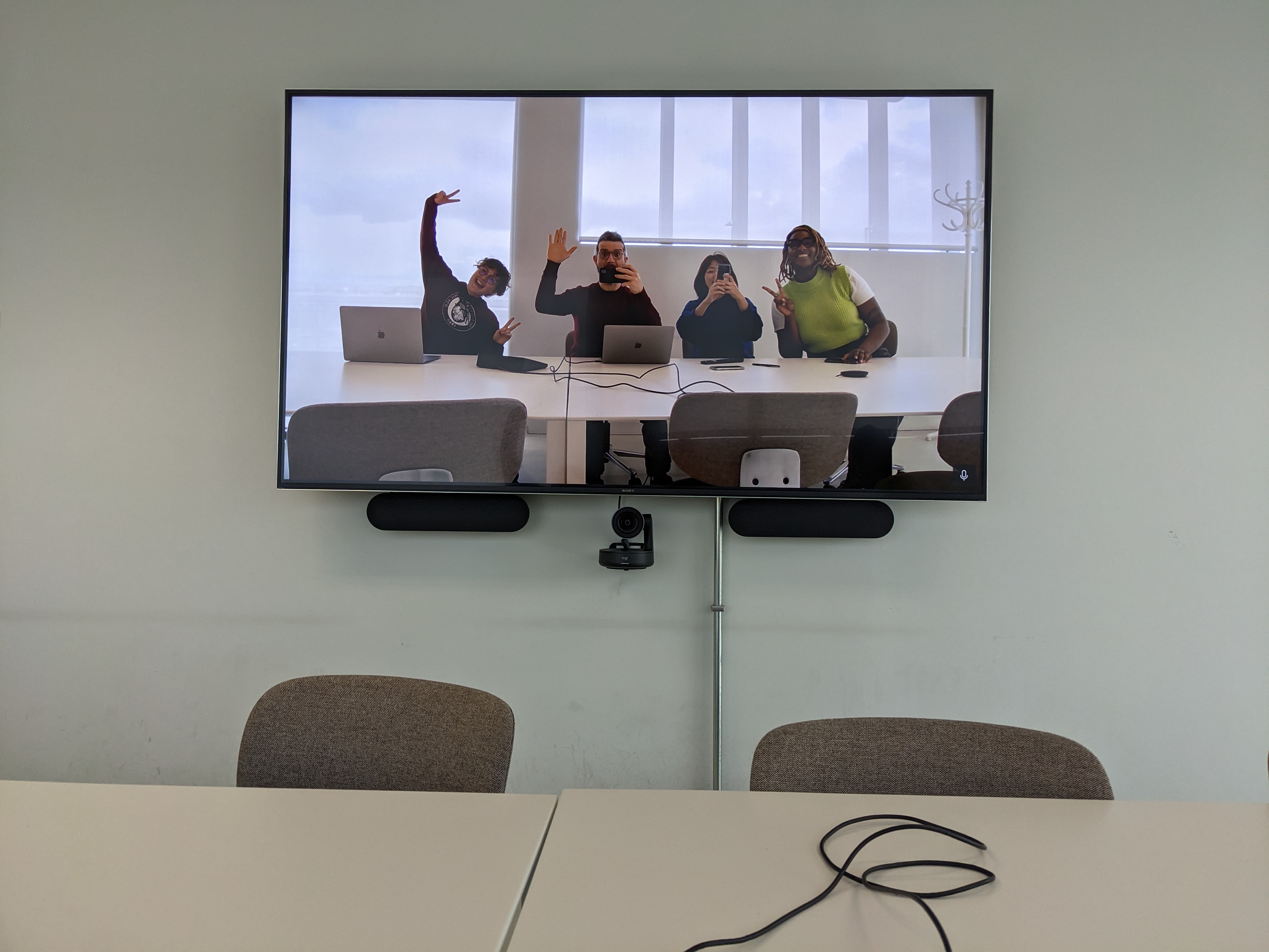 Écran de visioconférence affichant quatre collègues souriants autour d’une table avec ordinateurs portables.