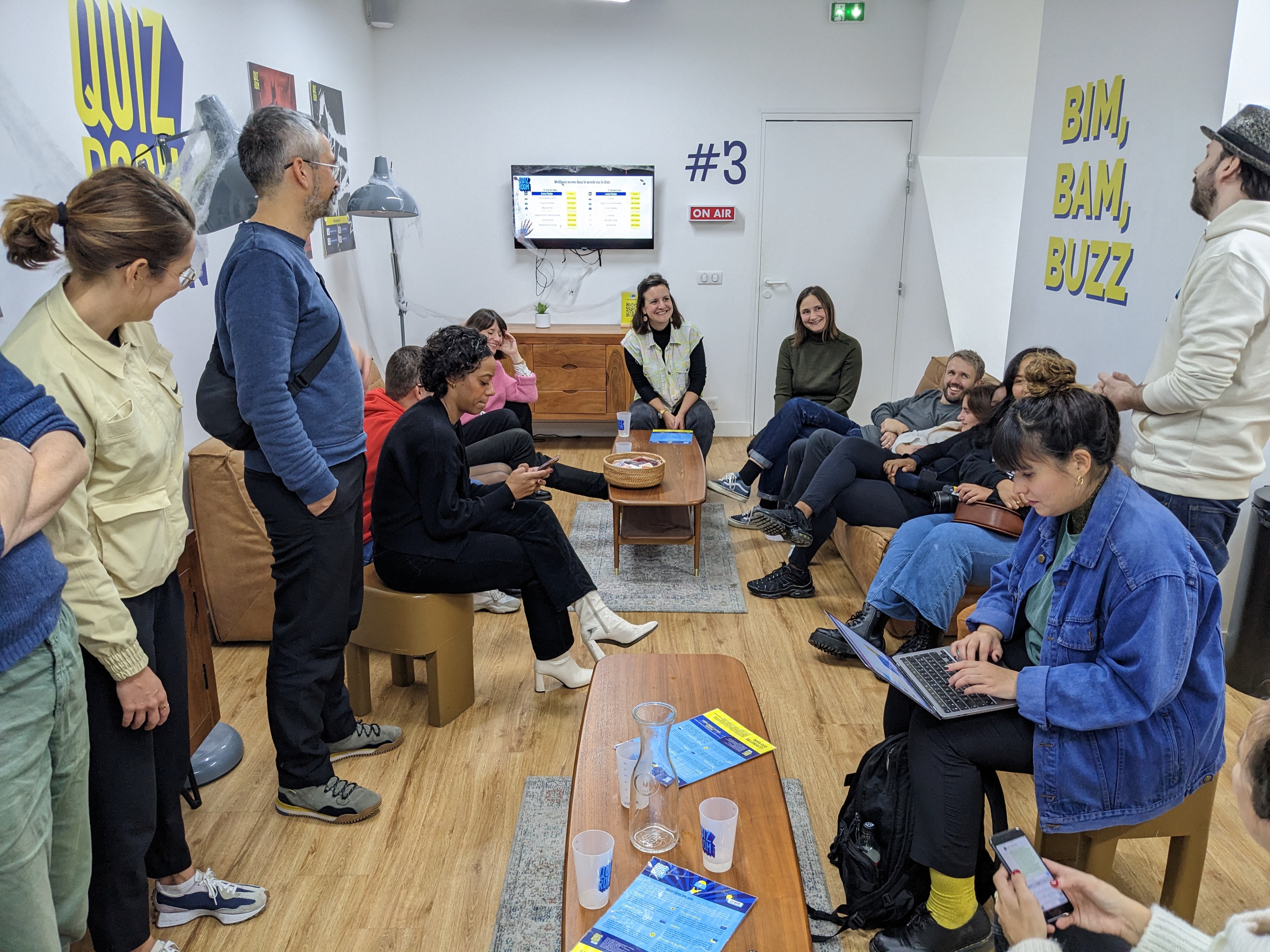 Groupe de collègues réunis dans un espace détente de bureau, assis sur des canapés autour d’une table basse.