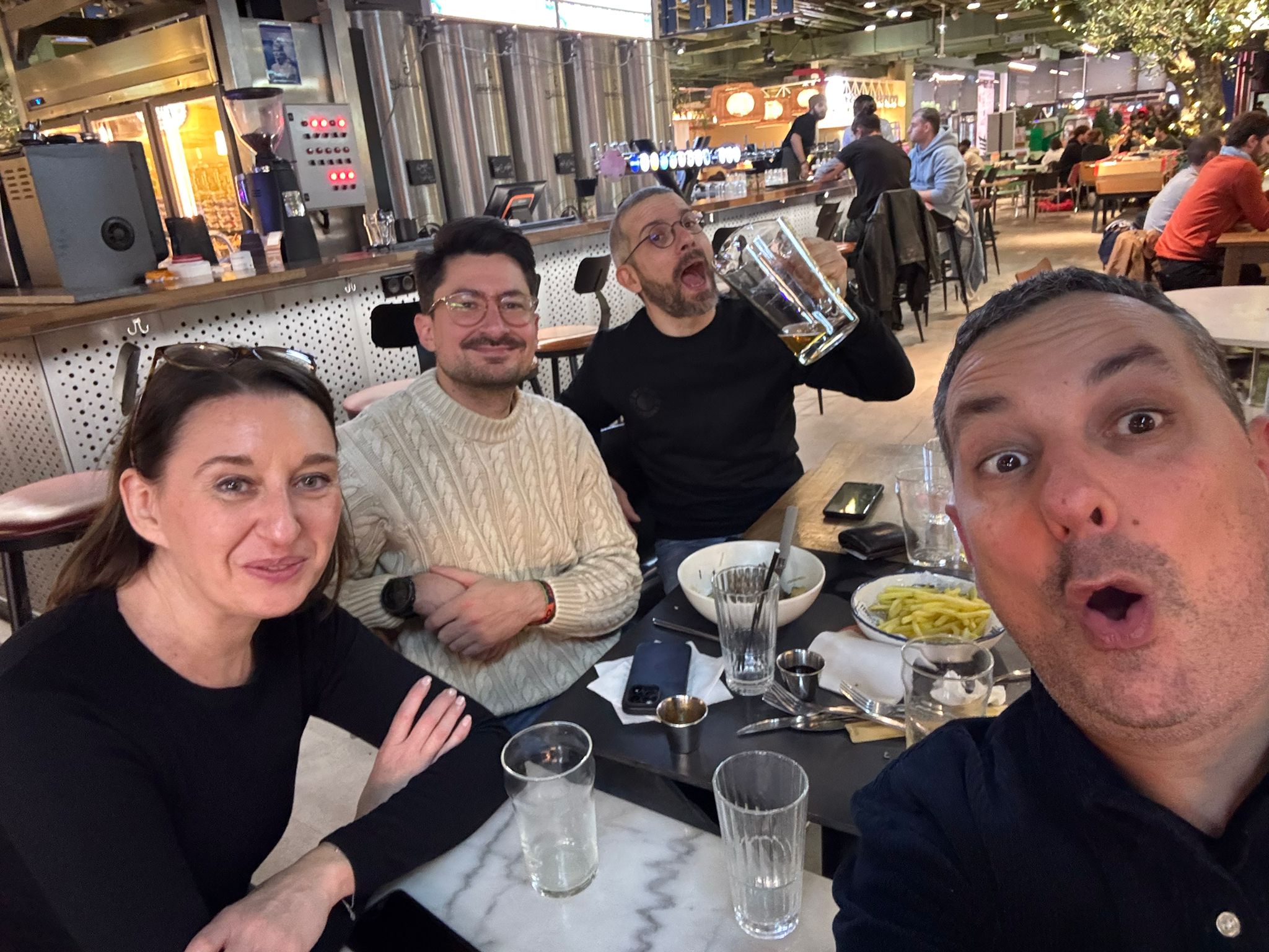 Selfie de quatre collègues attablés dans une brasserie, l’un levant une grande chope de bière.