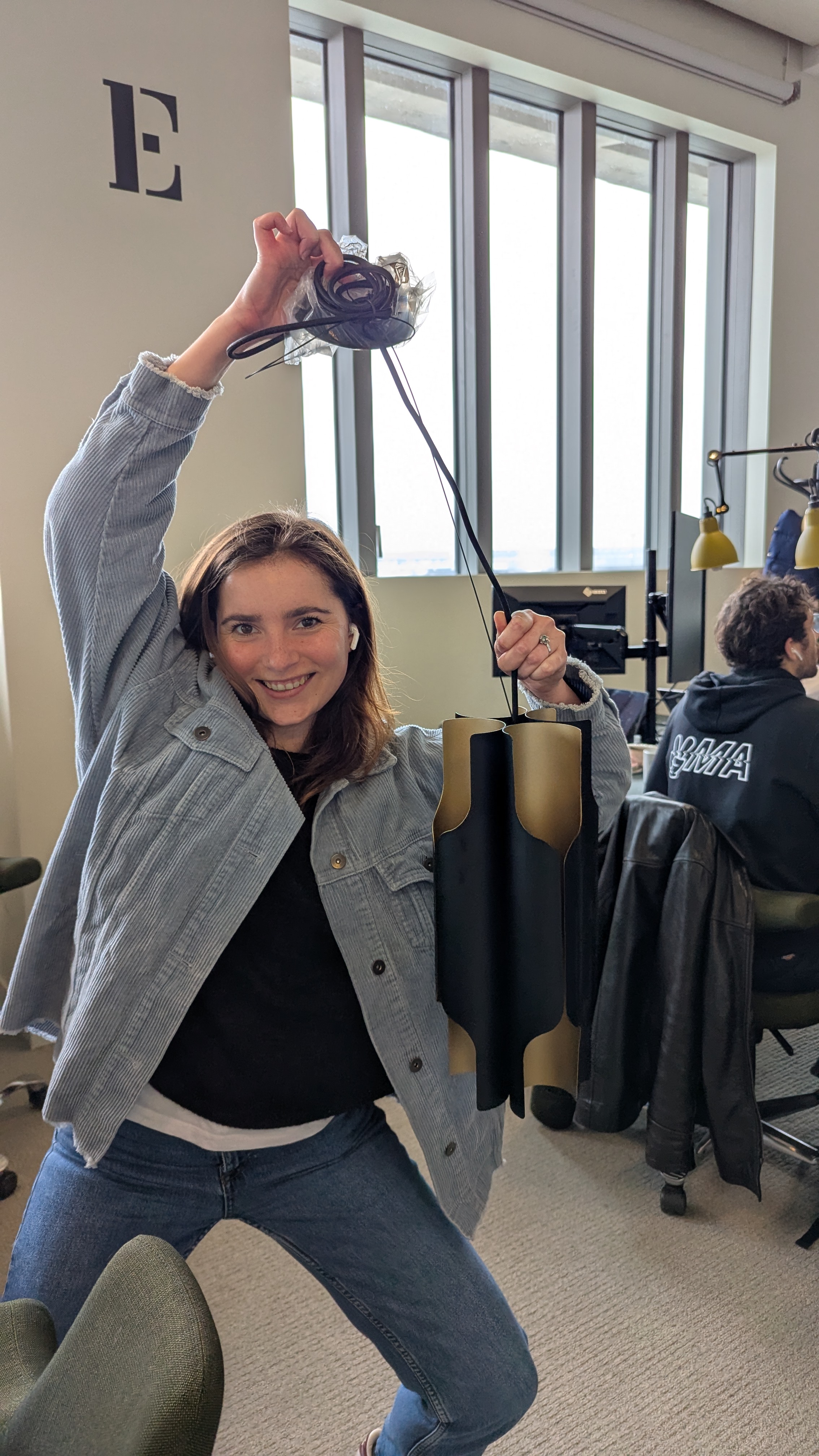 Femme souriante tenant une suspension lumineuse noire et dorée dans un bureau.