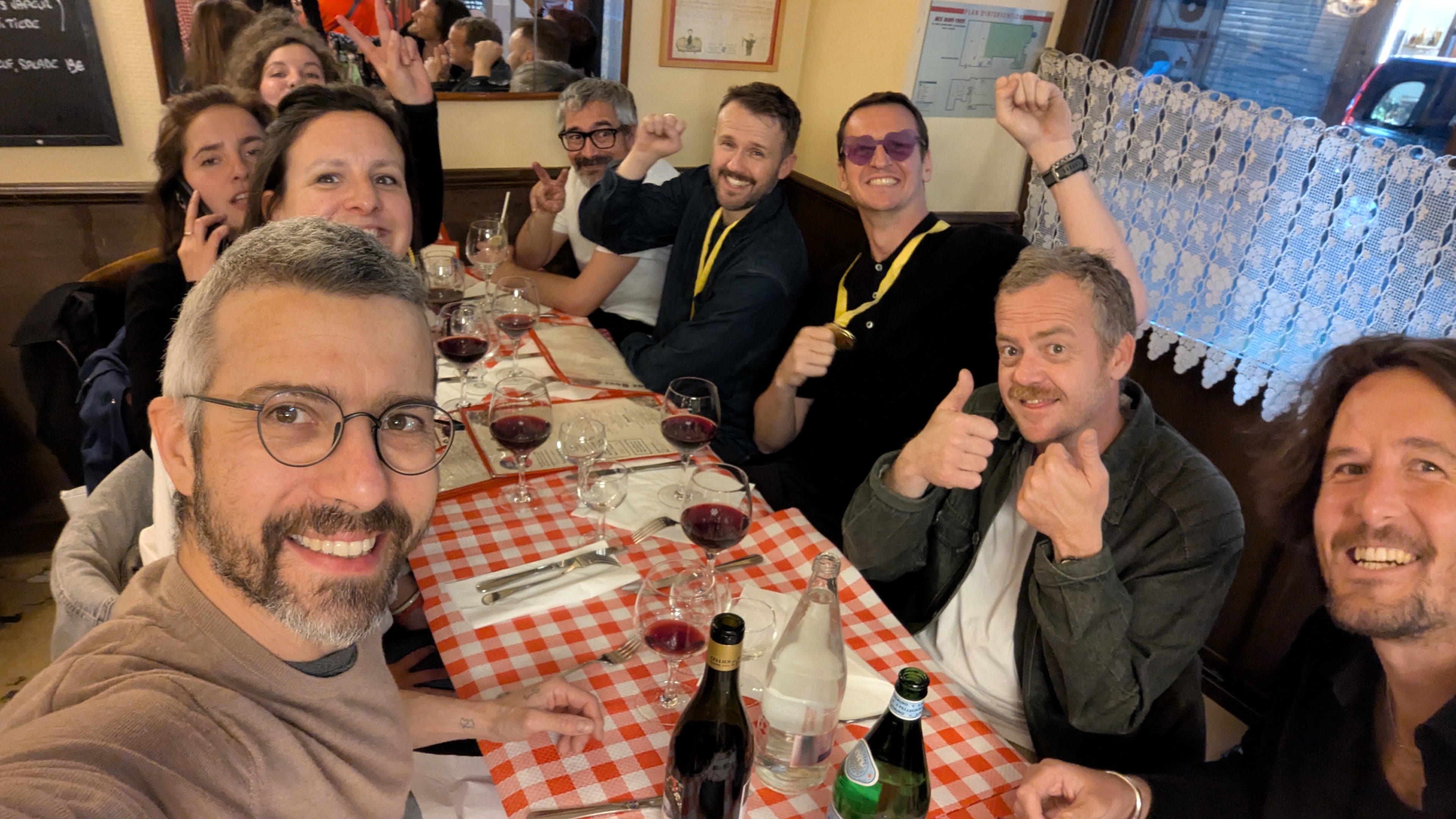 Selfie d’un groupe d’amis attablés dans un restaurant, verres de vin et bouteilles sur la table.